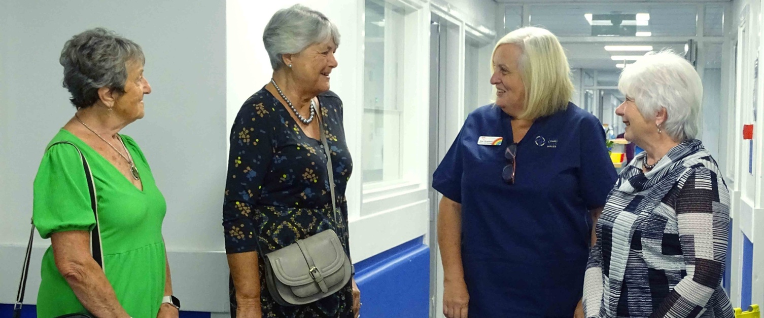 Image shows a group of people talking in a hospital corridor.