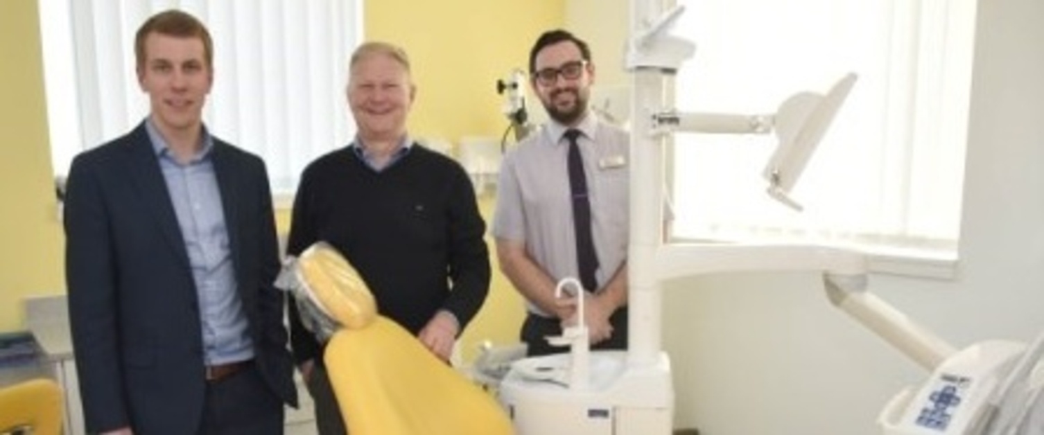 Three male staff members from a dental practice in Swansea stood around a dental chair.