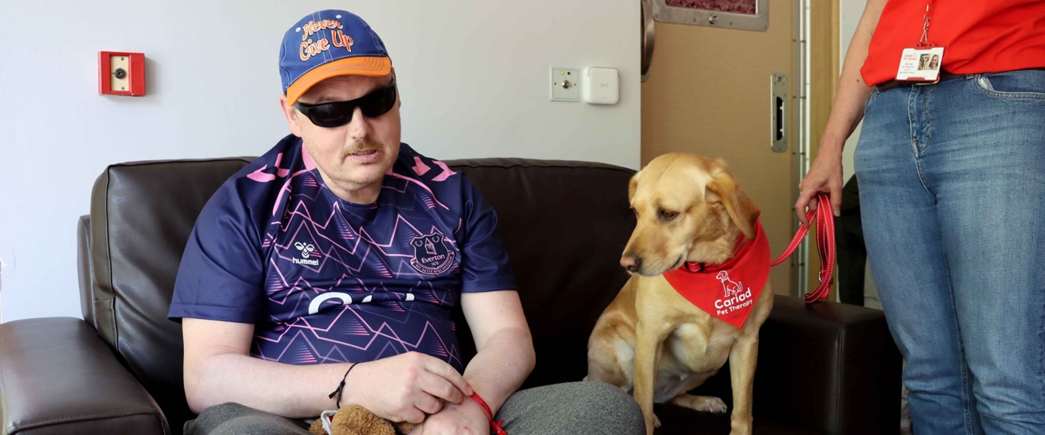 Image shows patient Jason sat on a sofa next to therapy dog Billie.