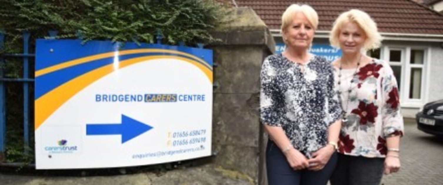 Two women support workers stood by a sign outside a Carer Centre in Bridgend.