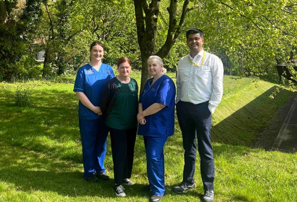 Image shows four people standing in a wooded area.