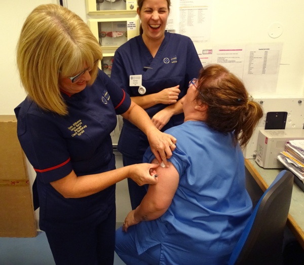 Picture of three happy nurses laughing together while one has a vaccination.