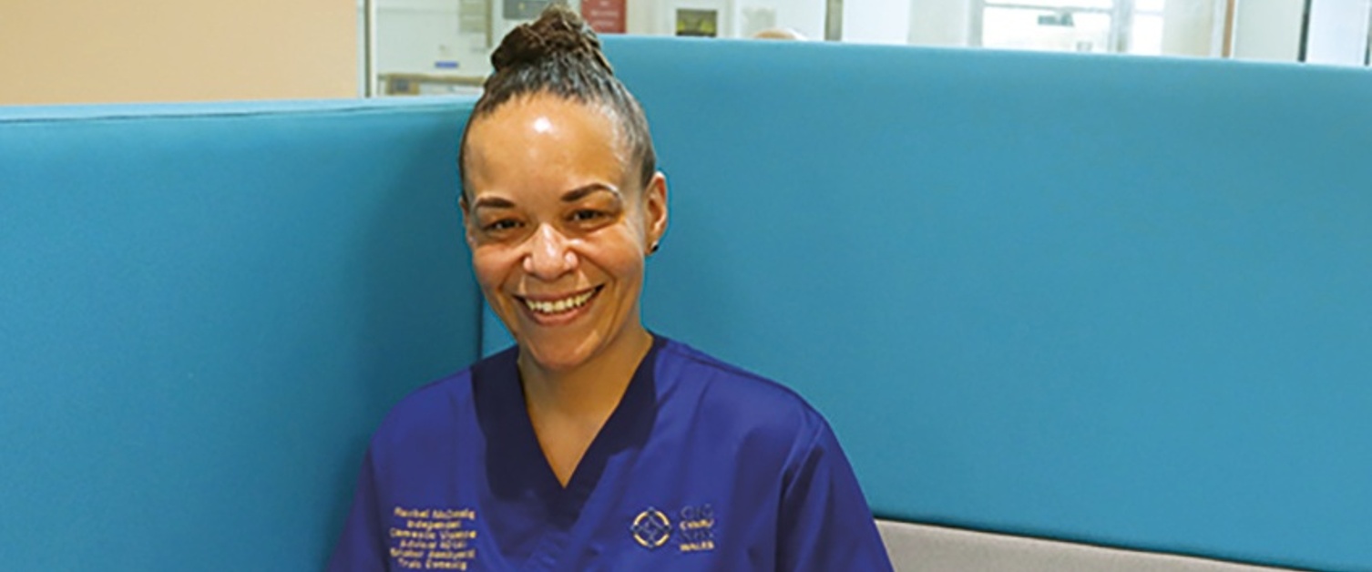 A smiling nurse sitting at a desk, with a laptop in front of her