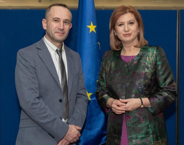 A smartly dressed man and woman standing in front of a European Union flag