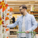 A man in a supermarket selects an item using his right arm.