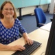 Image shows a woman sitting at a desk and holding her hands over a computer keyboard