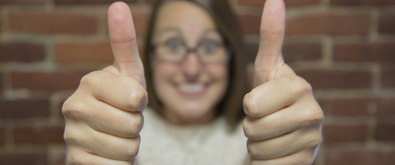 Woman smiling at camera with two thumbs up.