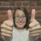 Woman smiling at camera with two thumbs up.