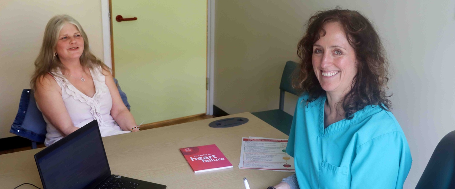 Patient Tracy pictured sitting at desk talking to pharmacist Kerys Thomas.