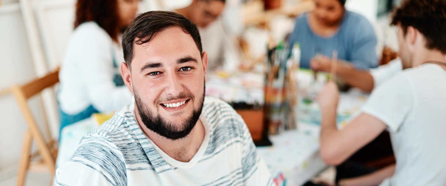 A smiling man. People behind him are painting around a table.