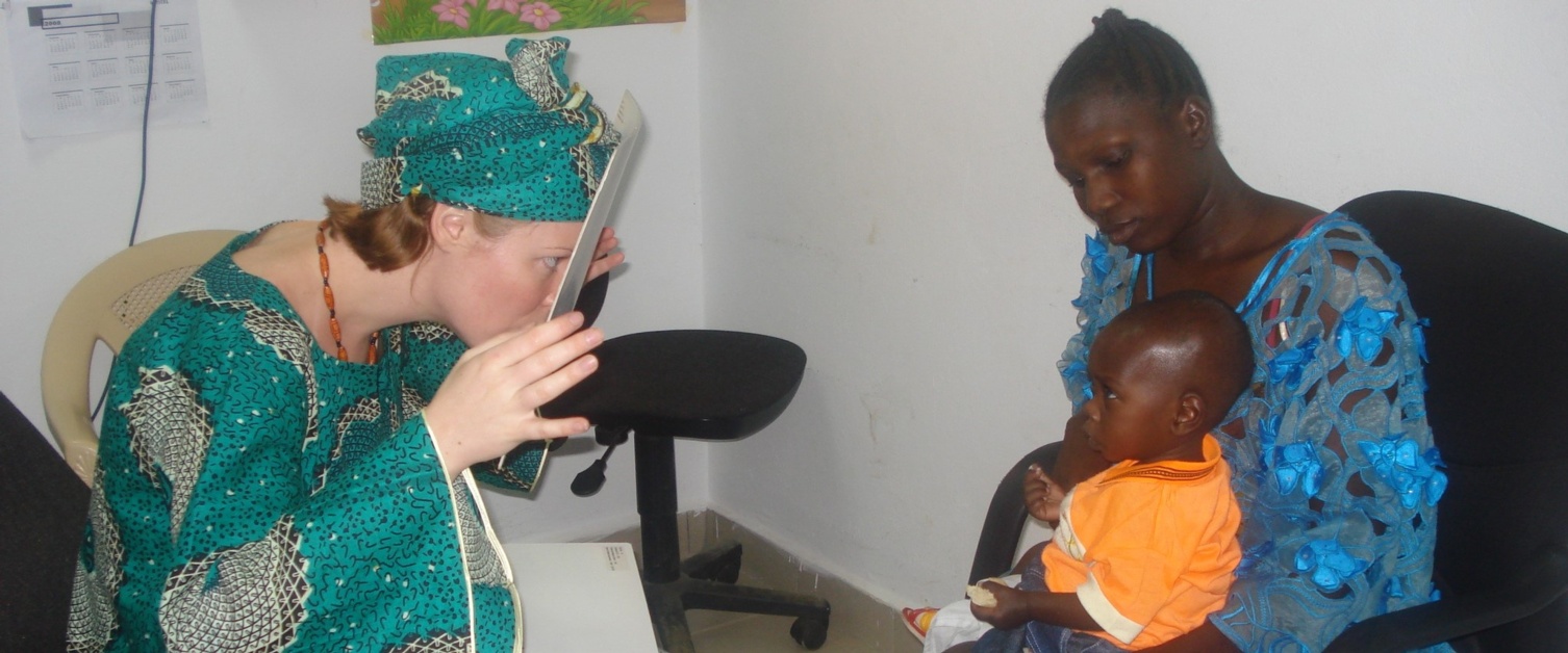 An image of a young person being held by his mother whilst having his eyes tested by a Orthoptist in Gambia
