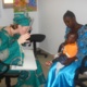 An image of a young person being held by his mother whilst having his eyes tested by a Orthoptist in Gambia