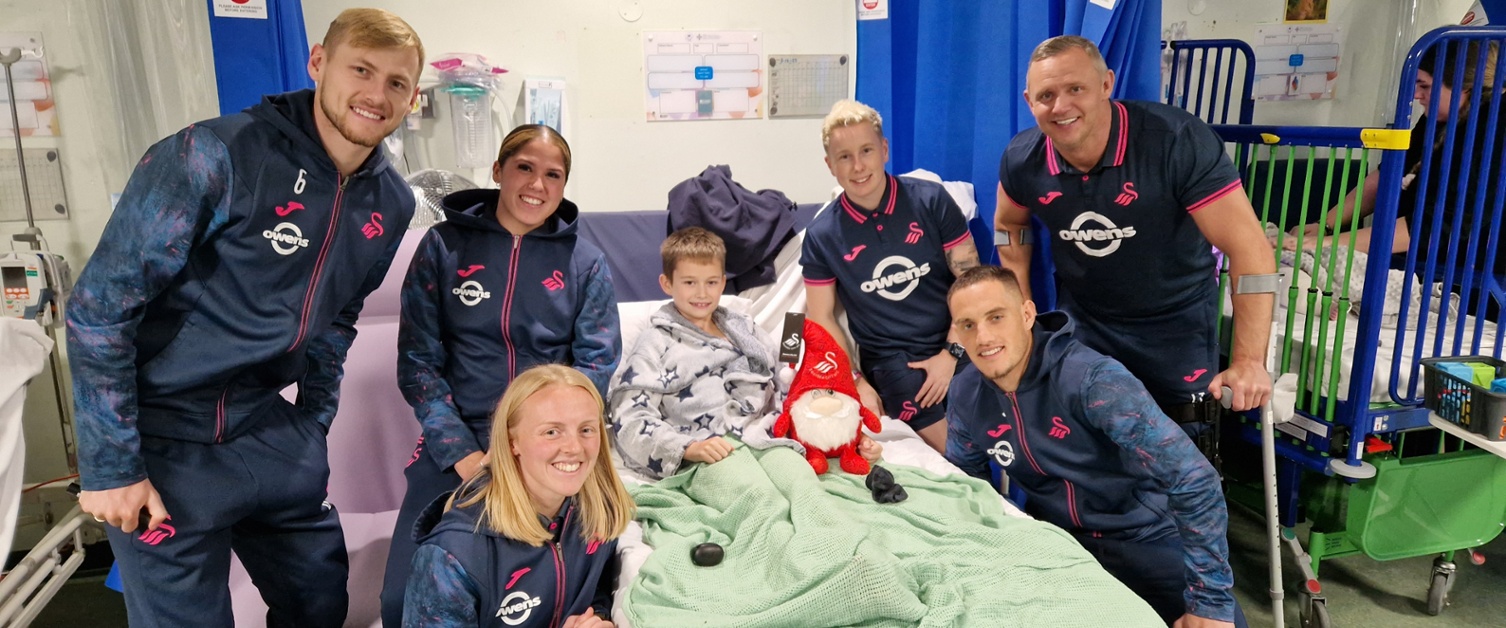 Image shows a group of people standing around a child in a hospital bed