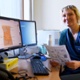 Dr Gemma Eccles yn dal darn o bapur yn agos at sgrin y cyfrifiadur