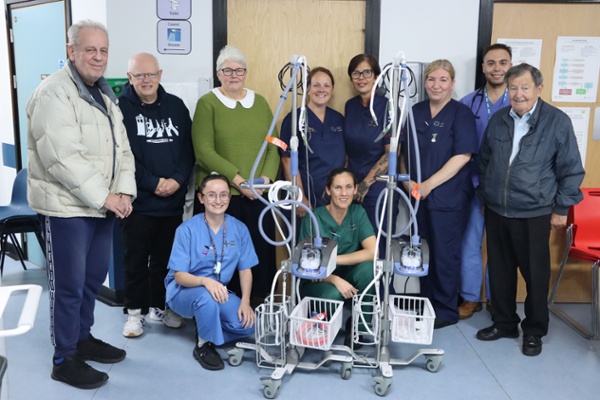 Grŵp o bobl a staff ysbyty yn sefyll o flaen rhywfaint o offer clinigol