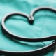 A stethoscope lying on green scrubs makes a heart shape.