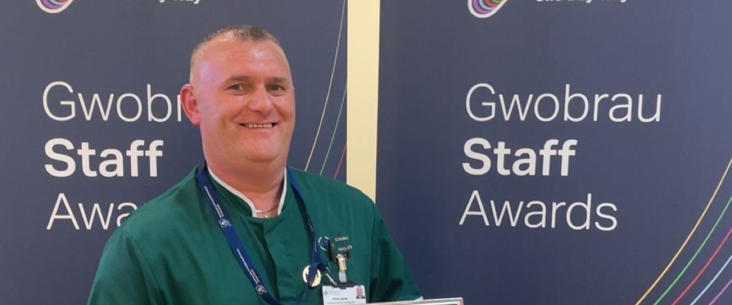 Steve yn gwisgo ei wisg ac yn dal ei dystysgrif wobr