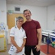 Ffisiotherapydd yn gwenu ac yn sefyll wrth ymyl claf blaenorol mewn ystafell ymgynghori