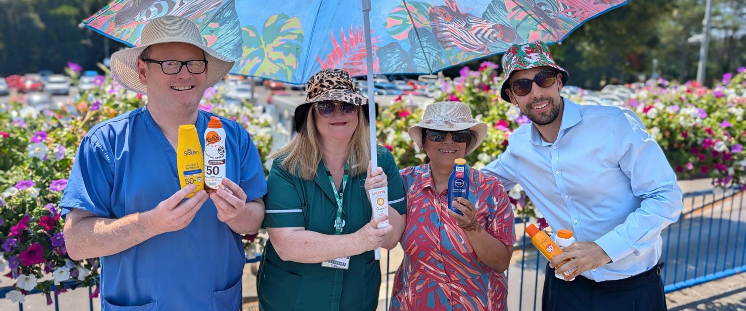 Grŵp o staff ysbyty, yn gwisgo hetiau haul ac yn cysgu dan parasol yn yr haul