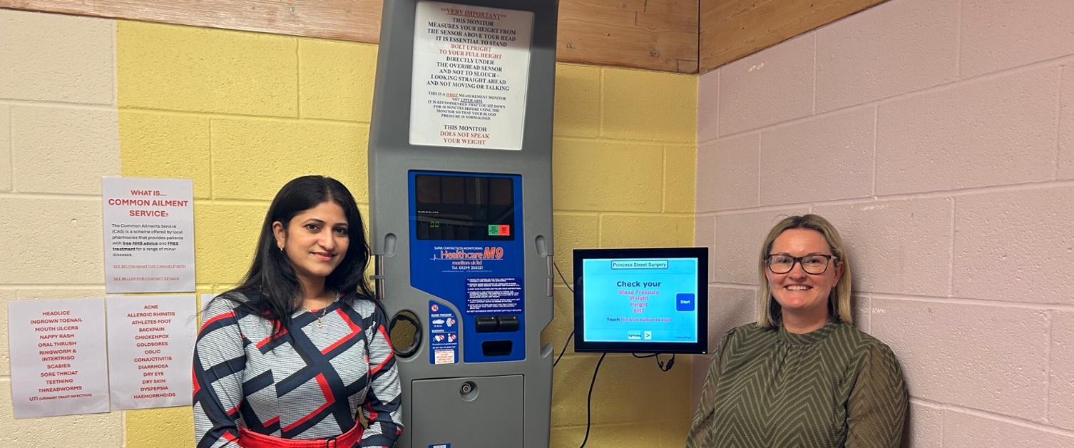 Sowndarya a Lorraine yn sefyll wrth ymyl y peiriant