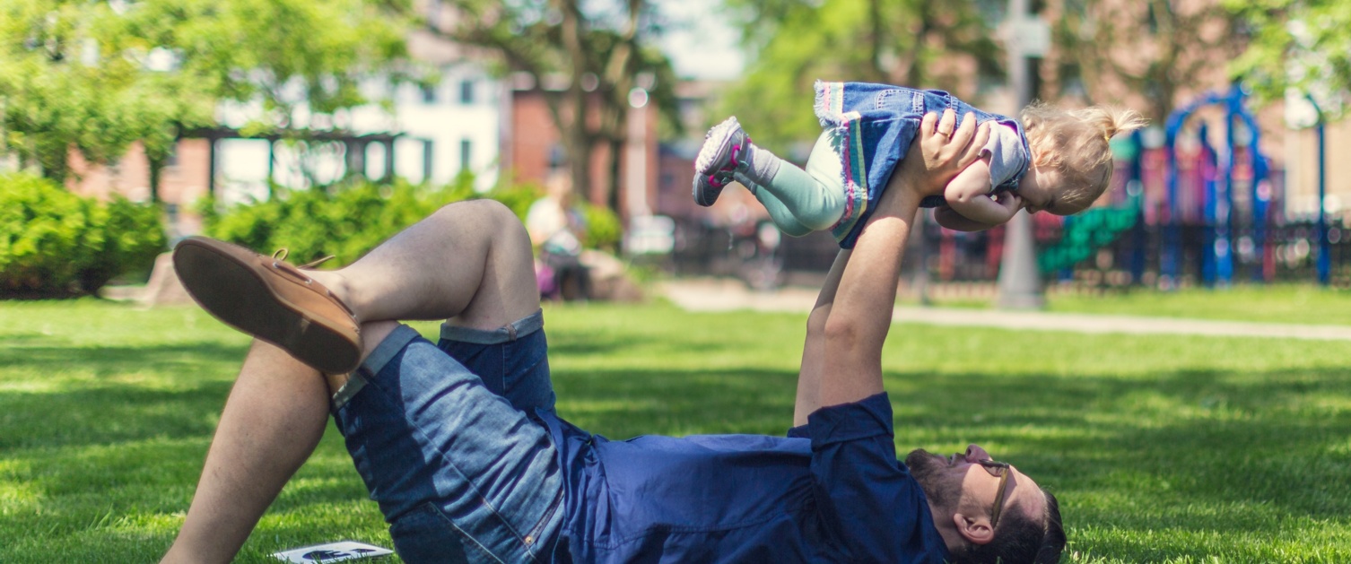 Picture of a man lying on grass holding a baby in the air.