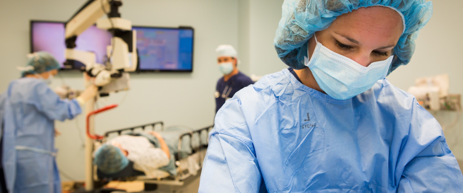Surgeon in foreground while surgery takes place behind