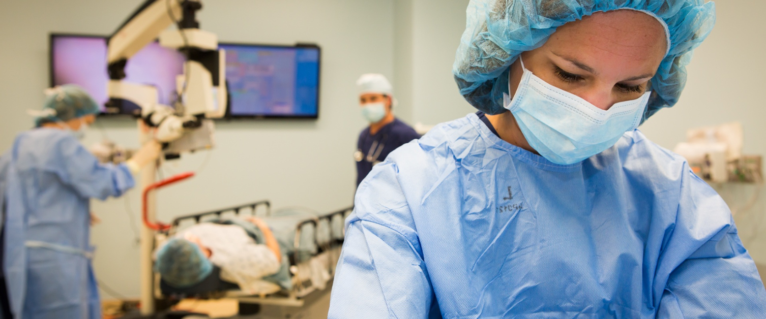 Surgeon in foreground while surgery takes place behind