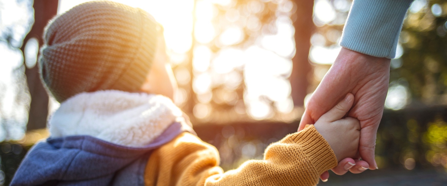 child holding adults hand while walking