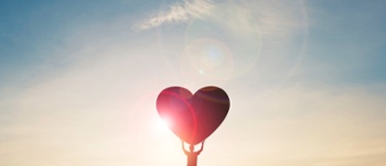 Person holding love heart with sunset