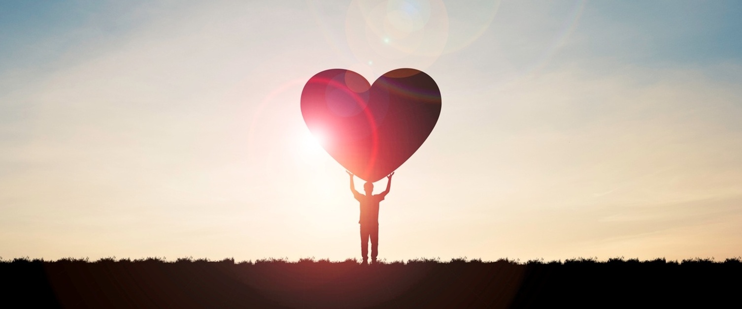 Person holding love heart with sunset