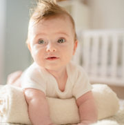 Baby lying on stomach over a rolled up towel to prop up their arms