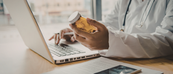 Doctor holding medication whilst using laptop