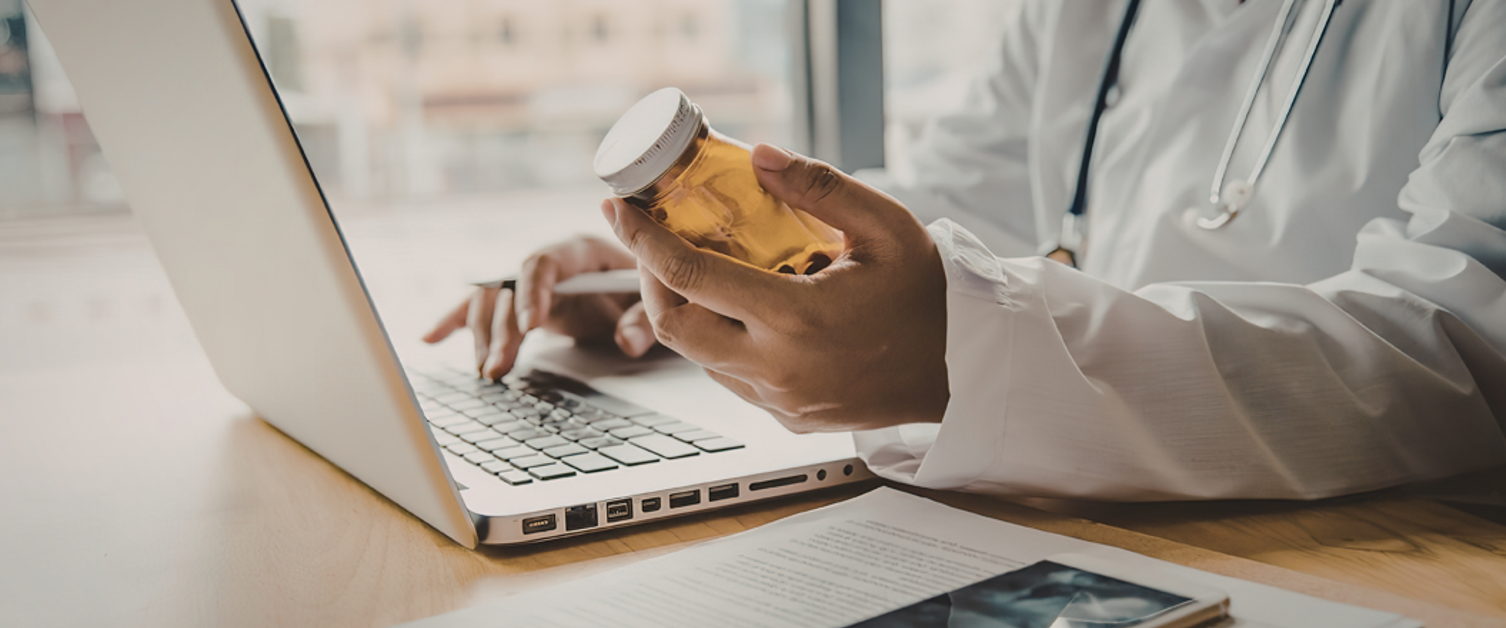 Doctor holding medication whilst using laptop