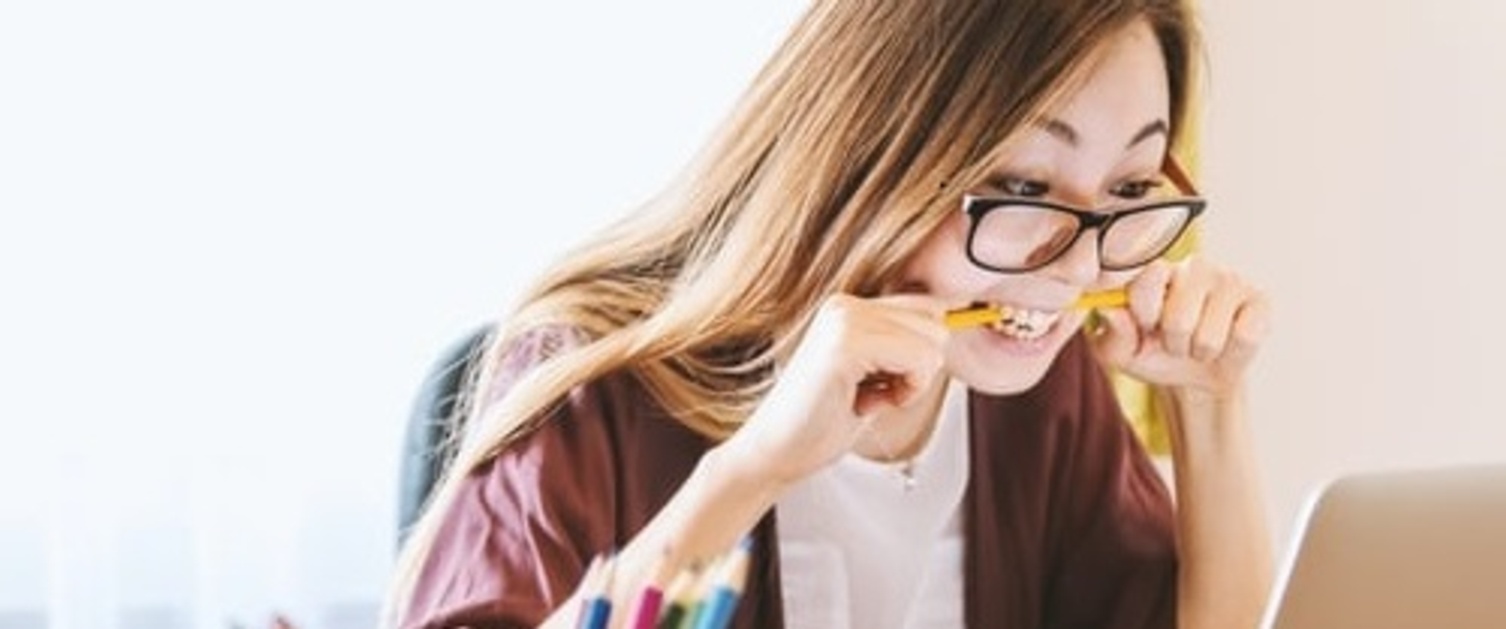 girl looking at computer screen with pencil in mouth