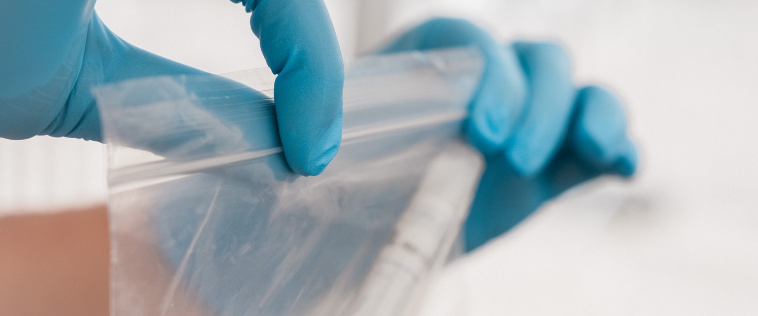 Gloved hands sealing a specimen into a bag