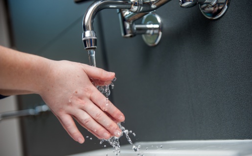 Image of someone rinsing their hands under a tap with a dark wall behind them