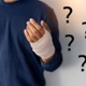 A person has a bandaged hand surrounded by question marks