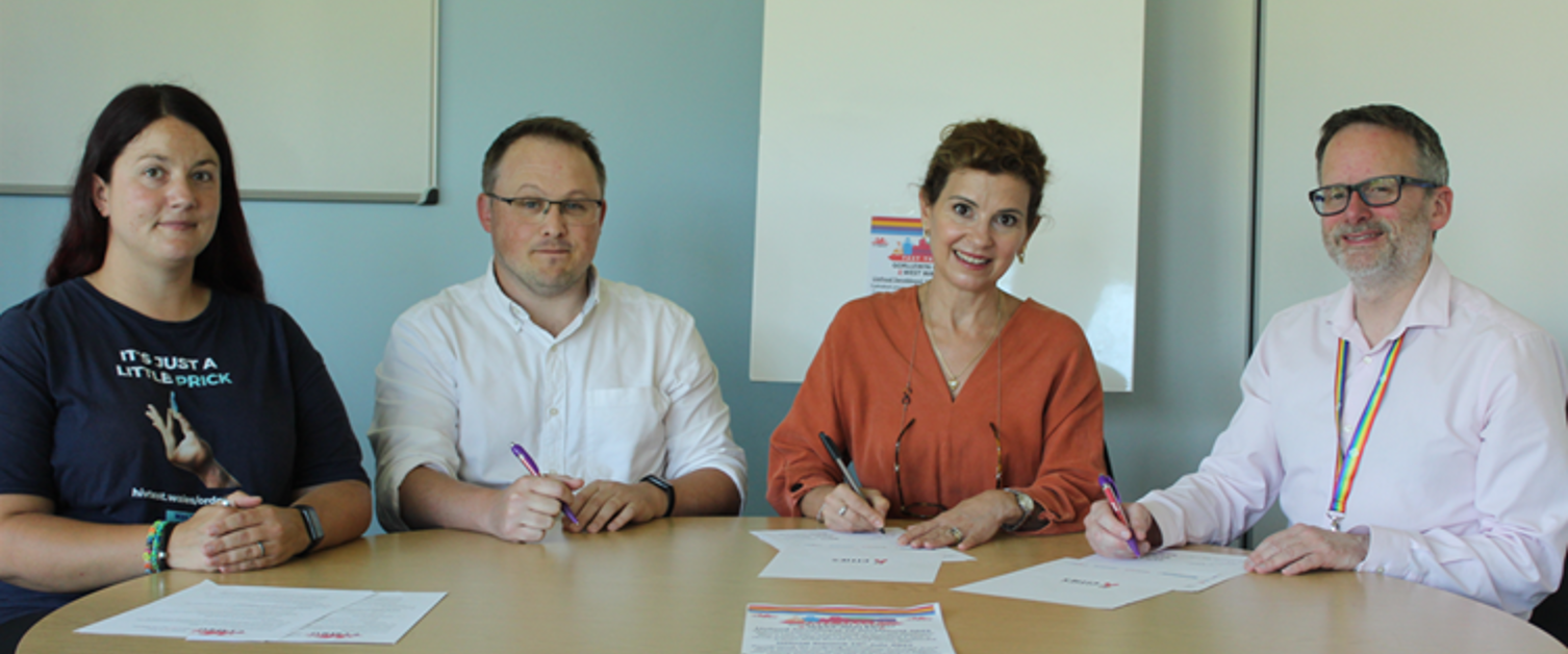 Addewid i weithio tuag at ddod â diwedd ar drosglwyddiad HIV erbyn 2030 People sitting at table signing paper