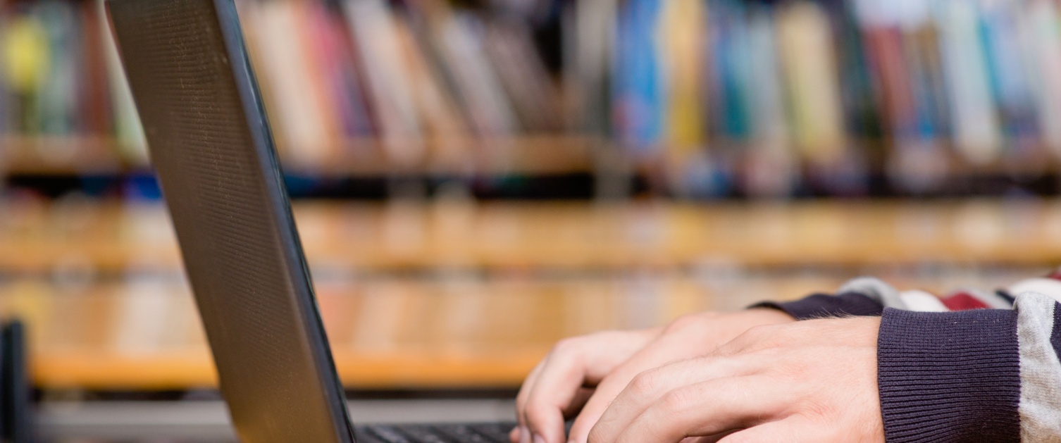 Hands typing on notebook in library