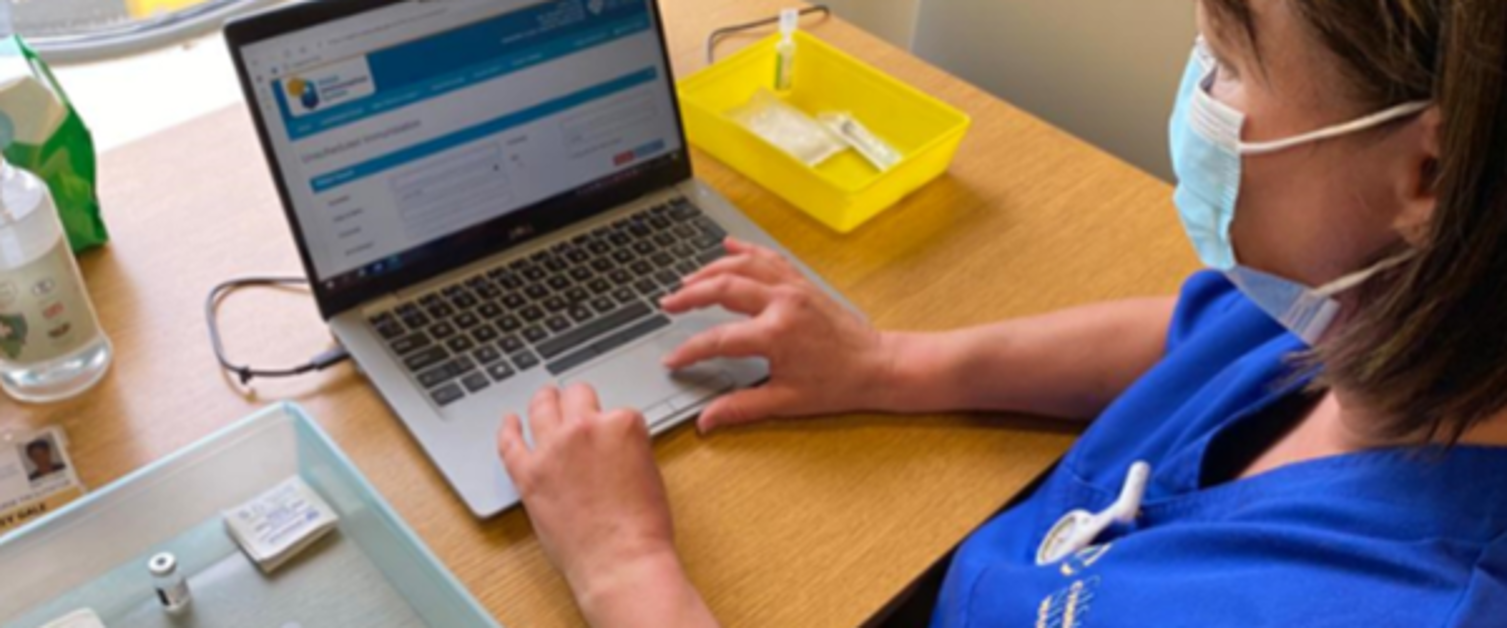 Nurse sat at laptop surrounded by medical equipment for vaccinations