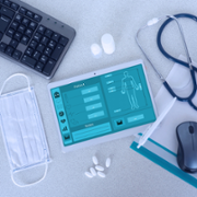 Medical equipment, like stethoscopes, pills and masks on a table with a digital screen, keyboard and mouse.