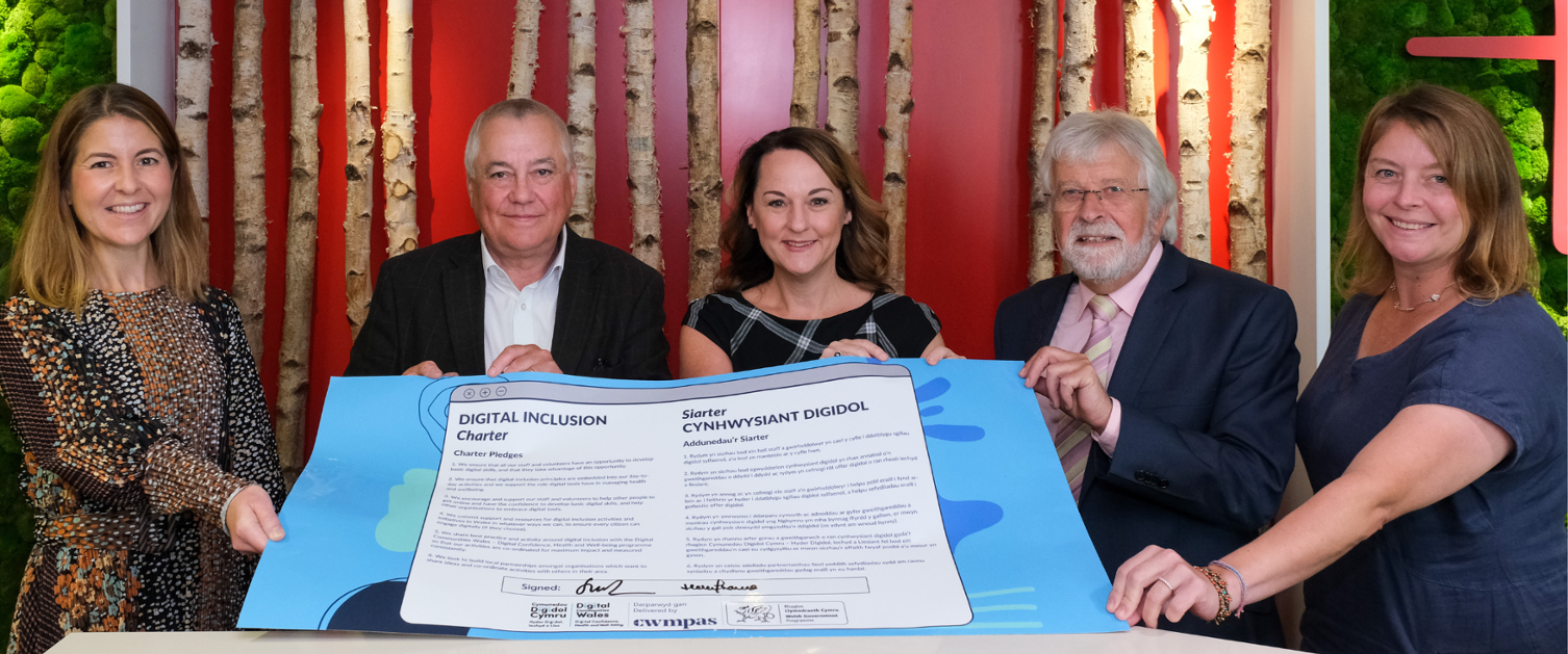 Representatives from Digital Health and Care Wales, Cwmpas and the Welsh Council for Voluntary Action hold a large, paper version of the Digital Inclusion Charter that