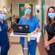 Helen Thomas, Chief Executive of Digital Health and Care Wales, stands with two nurses wearing blue scrubs who are stood at a laptop using the Welsh Nursing Care Record