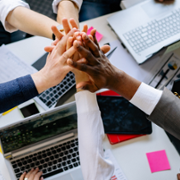 Five people giving each other a group high five over a table, over a laptop and post it notes.