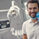 Dentist smiling at the camera wearing gloves and a mask, the background shows that he
