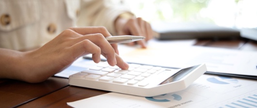 Individual using a calculator and holding a pen on a desk.