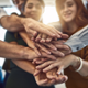 A group of friends all putting their hands into the middle on top of each other. 