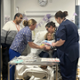 Example / scenario photo of mother with baby in hospital bed with midwives surrounding&nbsp;