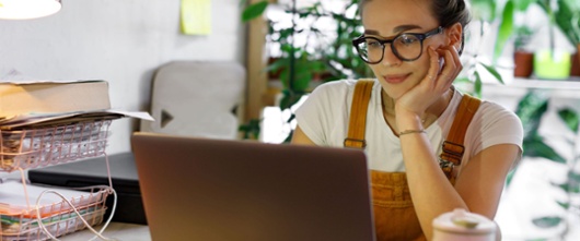 Woman wearing glasses, sitting at a desk using their laptop