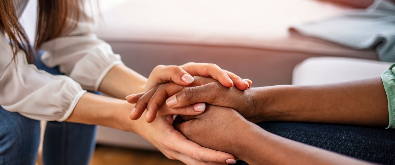 Two people clasping hands, sat opposite each other. 